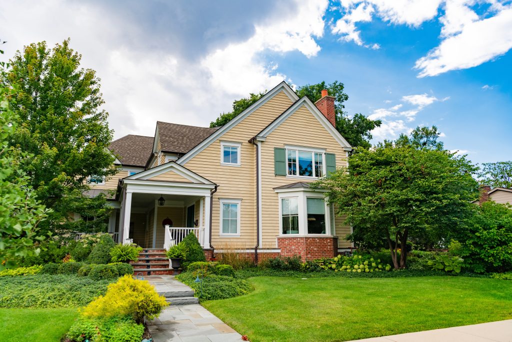 Yellow house with nice landscaping with a partly cloudy backdrop.